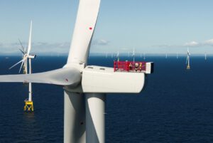 A close up image of the top of an offshore wind turbine, featuring 3 workers in fluorescent jackets working a red cage